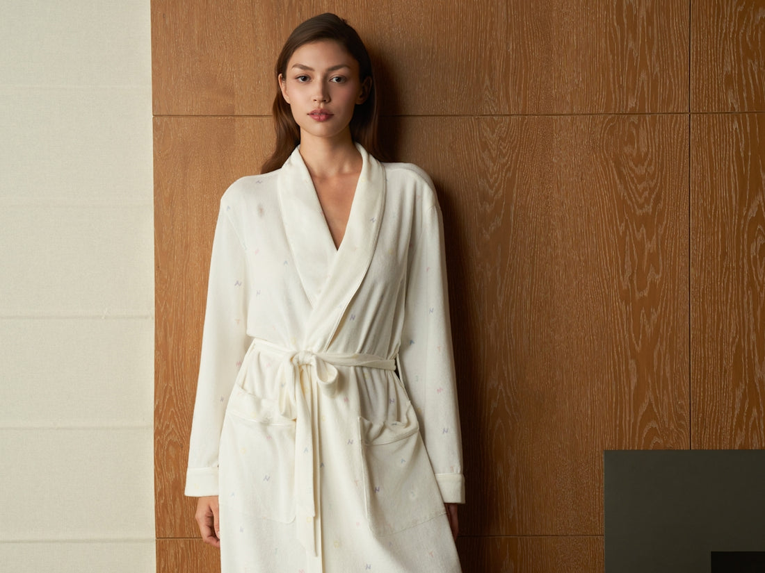 Woman wearing a white bathrobe standing against wooden wall