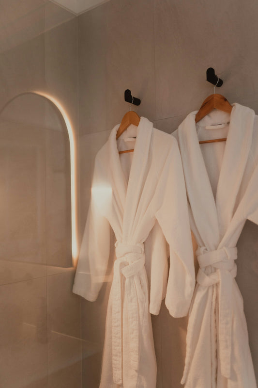 Two white bathrobes hanging on hooks in a modern bathroom.