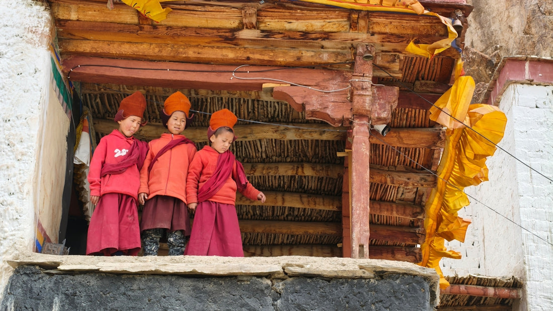 Three young monks in red robes on a wooden balcony.